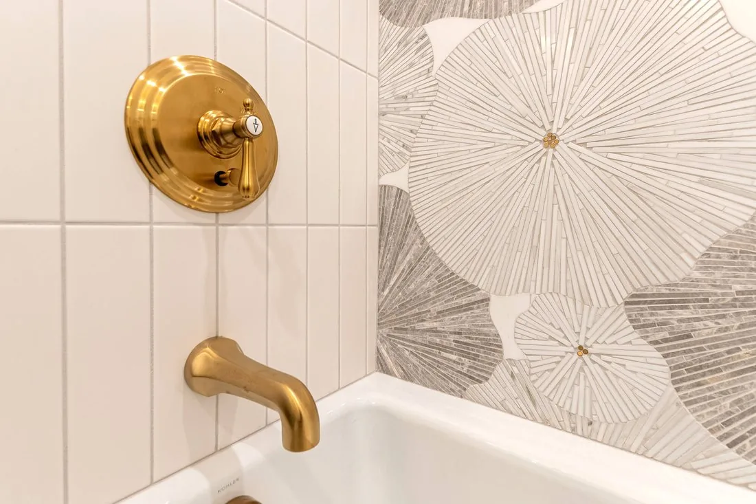 Brass tub filler set against patterned tile in a finished bathroom